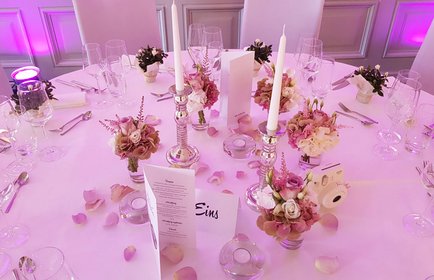 Elegant dekorierter Hochzeitstisch mit rosa Blumenschmuck, Kerzenleuchtern, Menükarte und romantischer Beleuchtung in festlichem Ambiente.