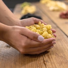 Frische Fusilli-Nudeln werden mit beiden Händen gehalten, auf rustikalem Holztisch – handgemachte Pasta als Symbol für italienische Kochkunst und Genuss.