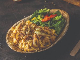 Hausgemachte Käsespätzle mit gerösteten Zwiebeln, serviert mit frischem Salat und Paprika auf rustikalem Holzteller.