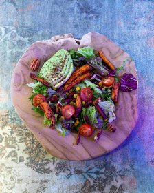Bunter Salat mit gegrilltem Ziegenkäse, Kirschtomaten, Karottensticks, Nüssen und Blattsalat auf rustikalem Holzteller – gesunde Bowl mit kreativem Streetfood-Touch.