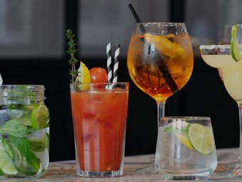 Verschiedene bunte Cocktails mit Limetten, Kräutern, Eis und Früchten auf einem Tisch, ideal für Sommerparty oder Barabend.