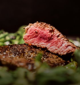Saftiges, medium gebratenes Steak auf einem Bett aus frischem Grün, nah aufgenommen für ein rustikales Streetfood-Erlebnis.