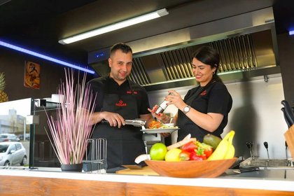 Zwei Mitarbeitende in einem modernen Foodtruck bereiten mit einem Lächeln frische Gerichte zu – freundlicher Service und hochwertige Streetfood-Küche mit frischen Zutaten.