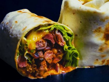 Saftiger Burrito mit Rindfleisch, Käse, Salat und Bohnenfüllung, angeschnitten auf dunklem Untergrund präsentiert.