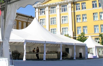 Großes weißes Eventzelt auf einem Stadtplatz vor historischem Gebäude, mit Buffet und sommerlicher Atmosphäre bei blauem Himmel.