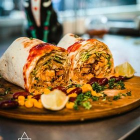 Frisch aufgeschnittener Burrito mit Hähnchen, Salat und Sauce, serviert auf Holzplatte mit Mais, Limette, Bohnen und Koriander – mexikanisches Streetfood voller Geschmack.