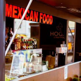 Detailaufnahme eines mexikanischen Streetfood-Foodtrucks mit Soßen, Deko und rotem Leuchtschild „Mexican Food“.