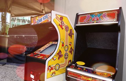 Zwei klassische Retro-Arcade-Spielautomaten im Freien, farbenfroh gestaltet mit Videospielmotiven, nostalgisches Gaming-Setup bei Sonnenschein.