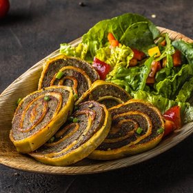 Vegetarische Rouladen aus Teig mit würziger Füllung, angerichtet mit frischem Salat aus Tomaten, Paprika und Blattsalat – serviert auf rustikalem Teller für Streetfood oder Event-Catering.