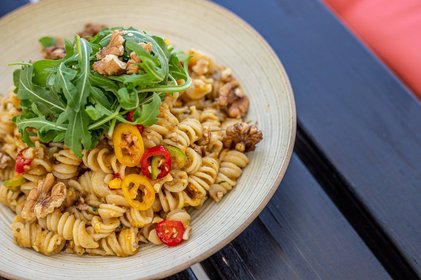 Pikante Fusilli-Pasta mit Walnüssen, Rucola und bunten Chilischoten auf Keramikteller – mediterrane Komposition mit Biss, ideal für Streetfood, Foodtruck-Menüs oder gesunde Küche.
