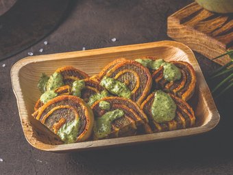 Gebackene Kartoffelspiralen mit Kräutersoße auf einem Holztablett, serviert auf dunklem Untergrund für rustikalen Streetfood-Look.