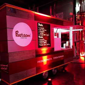 Stylischer Foodtruck „Pastsani“ mit beleuchteter Speisekarte für frische Pasta und Pinsa Romana, rot angestrahlt auf einem Indoor-Event – italienisches Streetfood modern inszeniert.