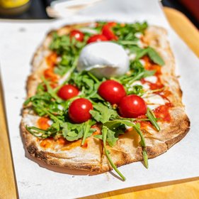 Frische Pizza mit Rucola, Cherrytomaten und Burrata auf knusprigem Teig, serviert auf Backpapier.
