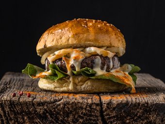 Saftiger Cheeseburger mit Rindfleischpatty, geschmolzenem Käse, Salat und Brioche-Brötchen auf rustikalem Holzuntergrund vor dunklem Hintergrund.