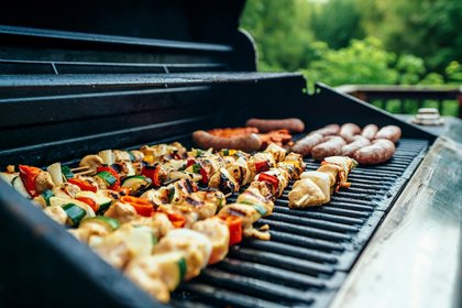 Gemüsespieße, Würstchen und Fleisch grillen auf einem heißen Grill im Garten mit grünem Hintergrund.