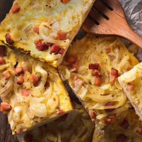 Frisch gebackener Zwiebelkuchen mit knusprigem Speck und goldbrauner Eimasse, in Stücke geschnitten und auf Holzuntergrund serviert – herzhafter Klassiker der Herbstküche.