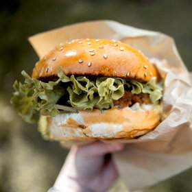 Frischer Chicken-Burger mit Sesambrötchen, grünem Salat und knusprigem Patty, gehalten in der Hand auf Streetfood-Event.