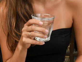 Frau in schwarzem Top hält ein Glas klares Wasser in der Hand, Nahaufnahme des Oberkörpers in entspannter Atmosphäre.