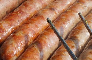 Goldbraun gegrillte Bratwürste auf einem Grillrost, Nahaufnahme bei direkter Hitze für typisches BBQ-Aroma.